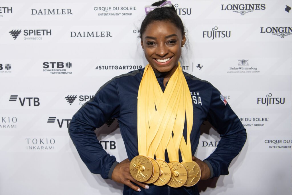 Here's an alt attribute for an image of Simone Biles wearing medals: Simone Biles wearing multiple medals and smiling.