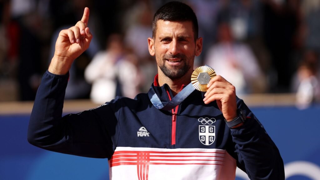 "Novak Djokovic holding and showing his gold medal after winning the men's singles at the Paris 2024 Olympics."